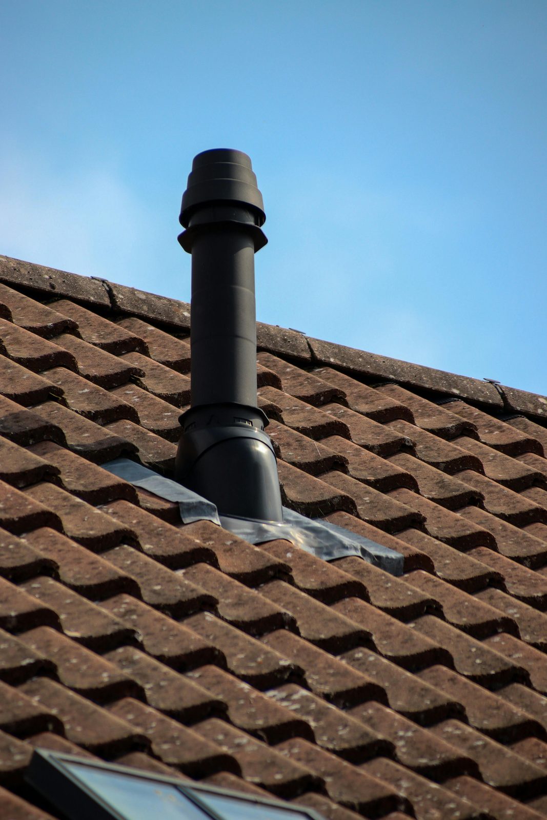Black vent pipe through a brown tiled roof
